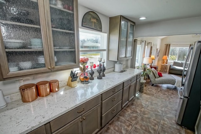 kitchen with recessed lighting, glass insert cabinets, freestanding refrigerator, light stone countertops, and dark tile patterned flooring