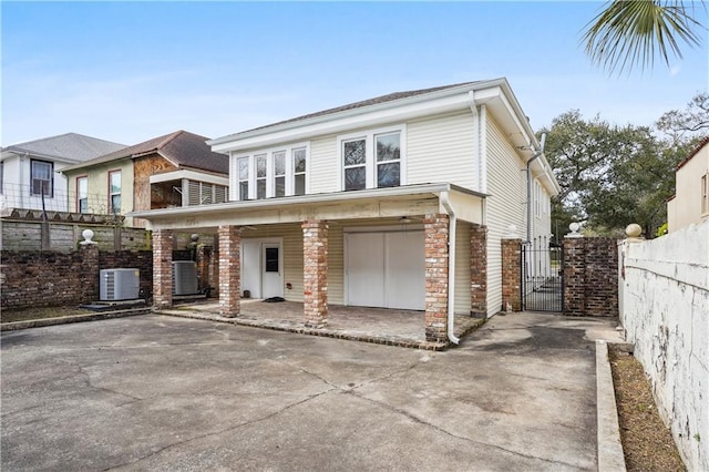 view of front of house with driveway, stone siding, a gate, fence, and central AC