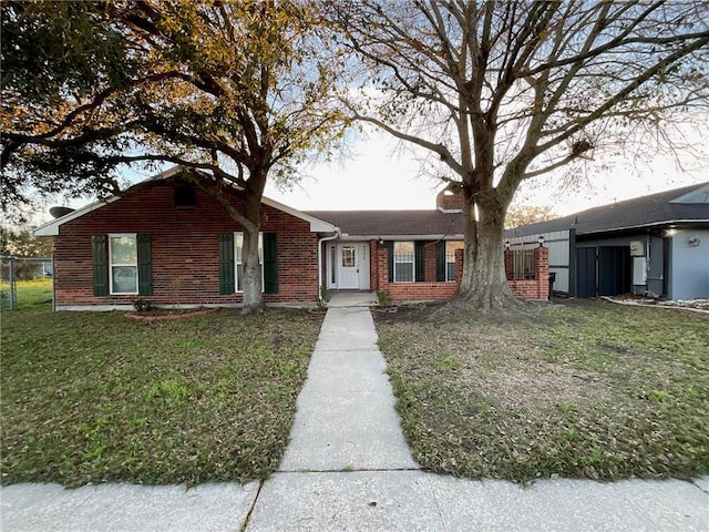 ranch-style home featuring a front yard, a chimney, and brick siding