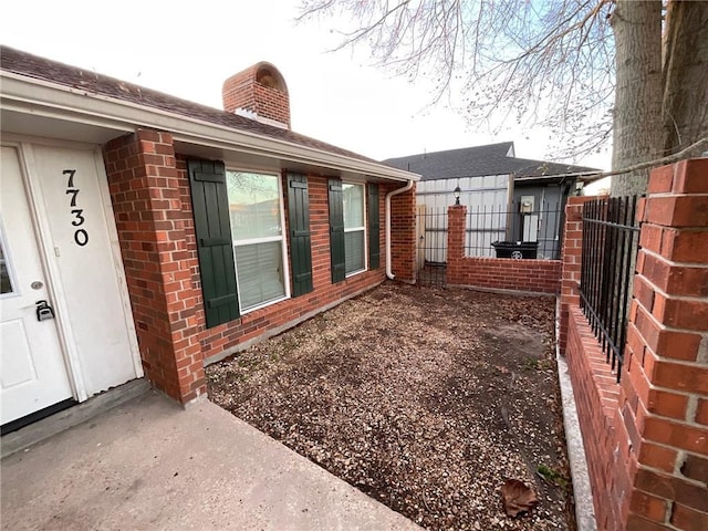 view of side of property with brick siding, fence, a chimney, and roof with shingles