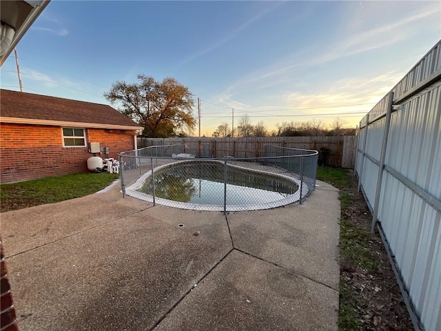 pool at dusk with a fenced backyard and a patio