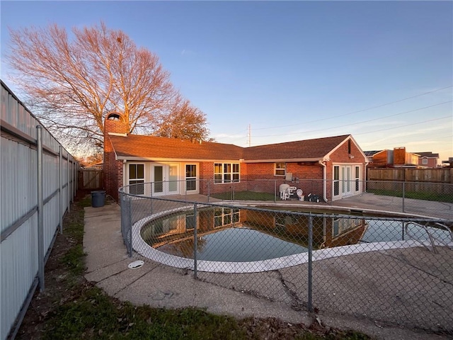 back of property at dusk featuring brick siding, a chimney, a fenced backyard, and a fenced in pool