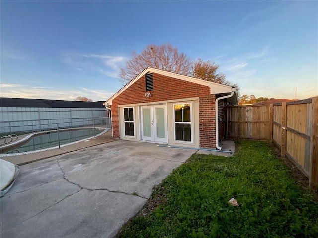 back of property with a patio, brick siding, a fenced backyard, and french doors