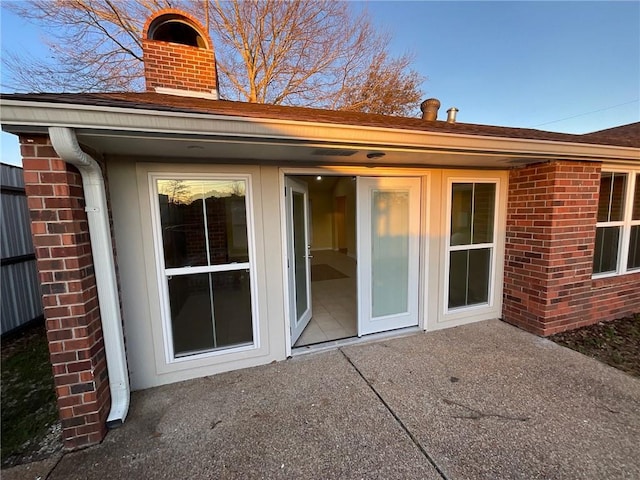 rear view of house featuring brick siding, a chimney, and a patio area