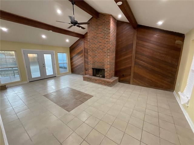 unfurnished living room with french doors, lofted ceiling with beams, a brick fireplace, light tile patterned flooring, and wooden walls