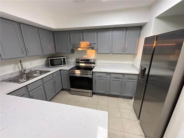 kitchen featuring light tile patterned floors, appliances with stainless steel finishes, gray cabinetry, under cabinet range hood, and a sink