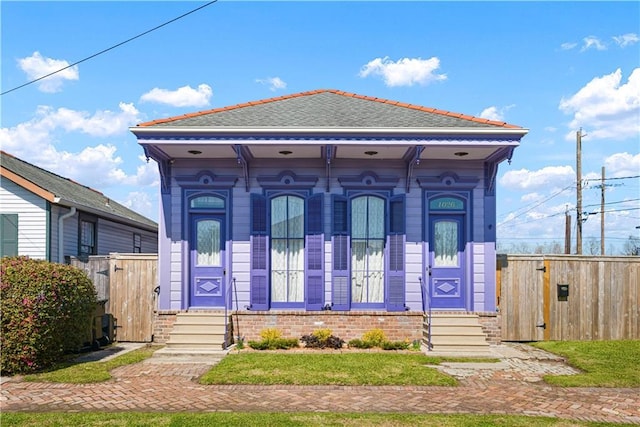 view of front of home with entry steps, brick siding, roof with shingles, and fence