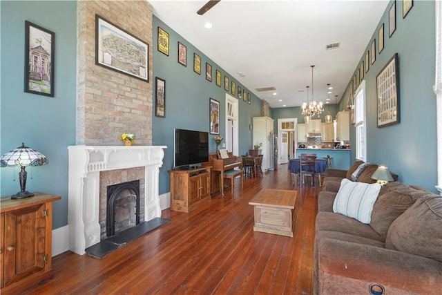 living area featuring a fireplace with raised hearth, recessed lighting, dark wood-type flooring, visible vents, and an inviting chandelier