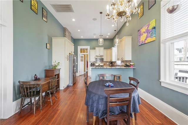 dining space featuring dark wood-type flooring, a high ceiling, visible vents, baseboards, and an inviting chandelier