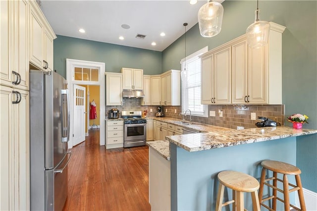 kitchen with under cabinet range hood, stainless steel appliances, a peninsula, visible vents, and cream cabinetry