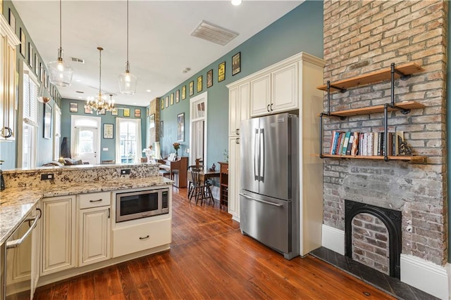 kitchen with cream cabinets, a fireplace, appliances with stainless steel finishes, and light stone counters