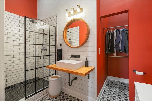 full bath featuring a shower stall, a spacious closet, baseboards, and a sink