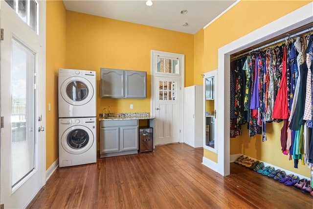 laundry area featuring cabinet space, baseboards, stacked washer / dryer, dark wood-type flooring, and a sink