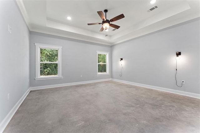 spare room with a raised ceiling, visible vents, a ceiling fan, concrete floors, and baseboards