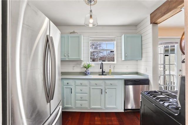 kitchen featuring wooden walls, stainless steel appliances, dark wood-style flooring, a sink, and light countertops