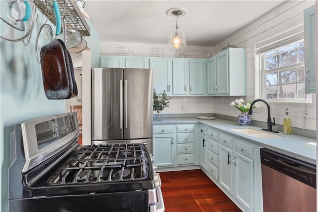 kitchen with stainless steel appliances, a sink, light countertops, dark wood-style floors, and decorative light fixtures