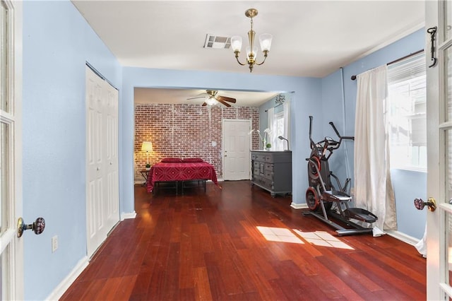 unfurnished bedroom with brick wall, wood-type flooring, visible vents, and an inviting chandelier