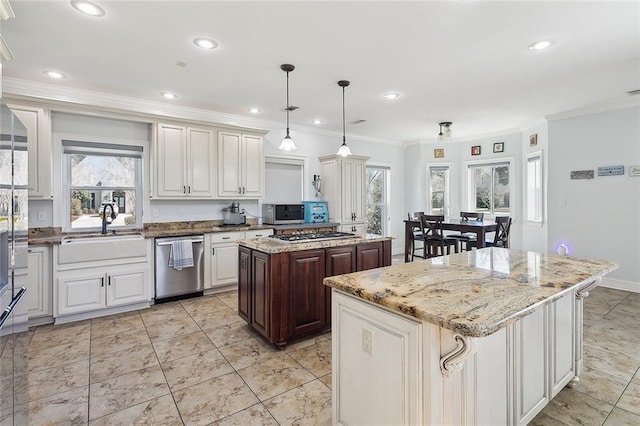 kitchen with a sink, a center island, appliances with stainless steel finishes, light stone countertops, and crown molding