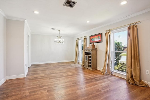 empty room featuring a healthy amount of sunlight, visible vents, a notable chandelier, and wood finished floors