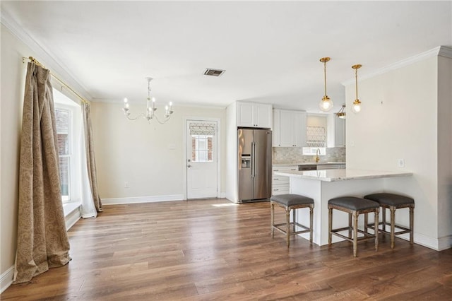 kitchen with a kitchen breakfast bar, stainless steel refrigerator with ice dispenser, backsplash, dark wood-style floors, and crown molding