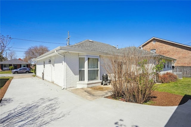 view of side of property with a patio, roof with shingles, fence, a yard, and brick siding