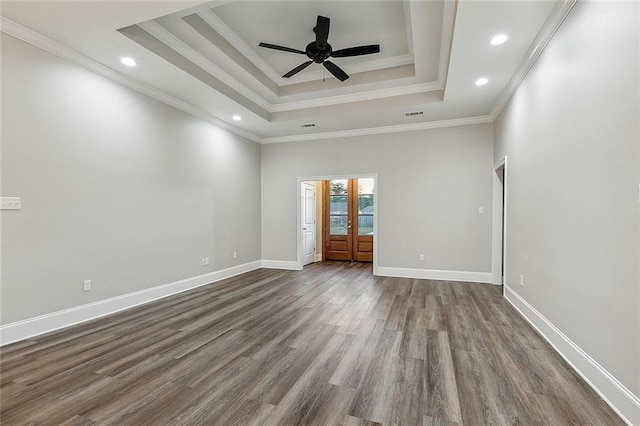 empty room with a raised ceiling, dark wood-type flooring, and ornamental molding