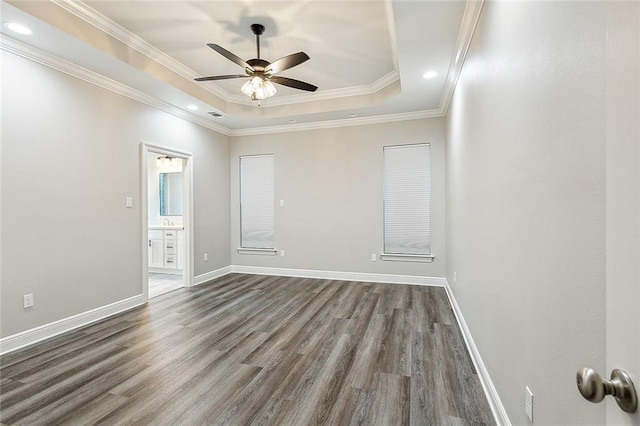 empty room with ornamental molding, a ceiling fan, a tray ceiling, wood finished floors, and baseboards