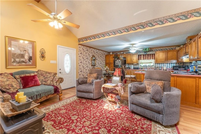 living area with ceiling fan, vaulted ceiling, light wood-style flooring, and wallpapered walls