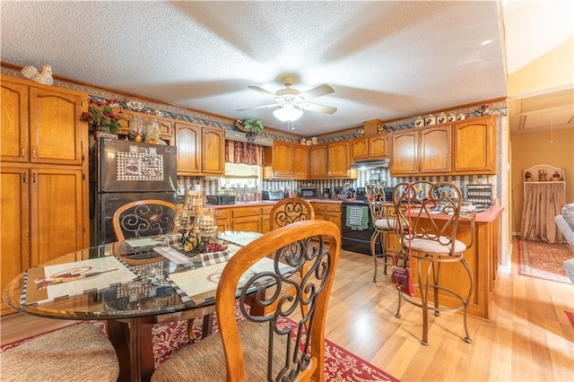 kitchen with brown cabinetry, freestanding refrigerator, light wood-style floors, and ceiling fan