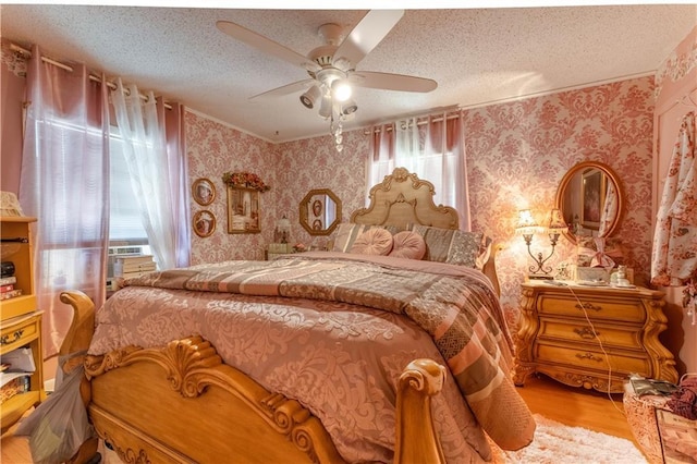 bedroom with a textured ceiling, ceiling fan, wood finished floors, and wallpapered walls