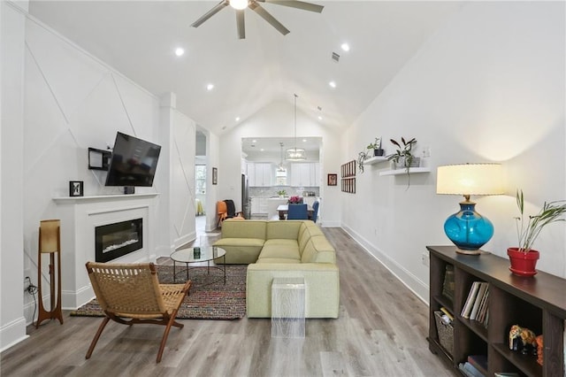 living area featuring a glass covered fireplace, ceiling fan, wood finished floors, high vaulted ceiling, and recessed lighting