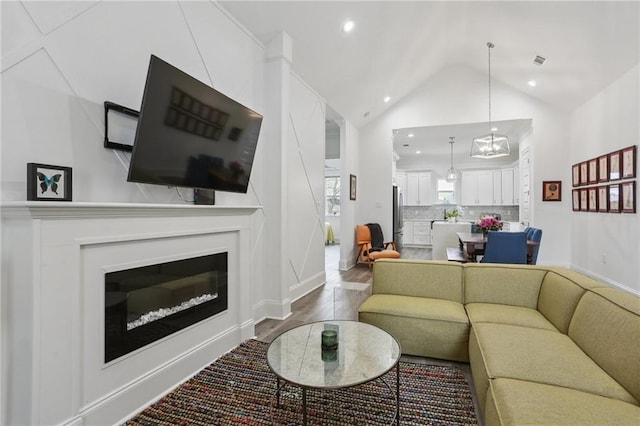 living area featuring recessed lighting, visible vents, a glass covered fireplace, vaulted ceiling, and wood finished floors