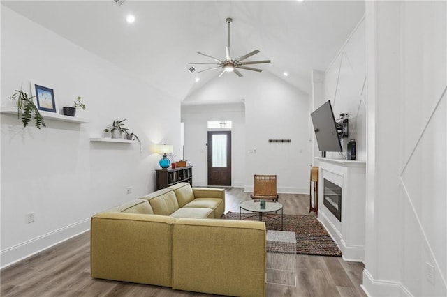 living area featuring a ceiling fan, a glass covered fireplace, wood finished floors, high vaulted ceiling, and recessed lighting