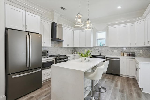 kitchen with a breakfast bar area, light countertops, appliances with stainless steel finishes, ornamental molding, and wall chimney range hood