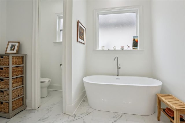 full bathroom featuring a healthy amount of sunlight, marble finish floor, baseboards, and a freestanding bath