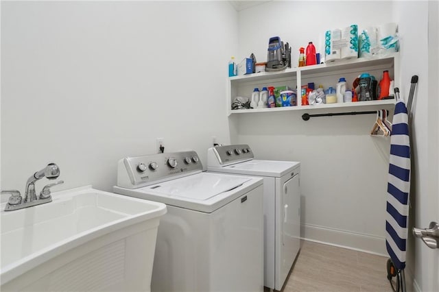 laundry room with light wood finished floors, washing machine and clothes dryer, a sink, laundry area, and baseboards