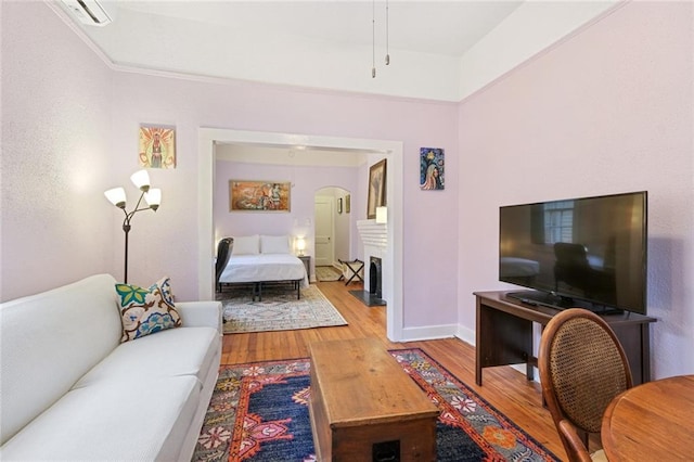 living area with arched walkways, a fireplace, wood finished floors, and baseboards