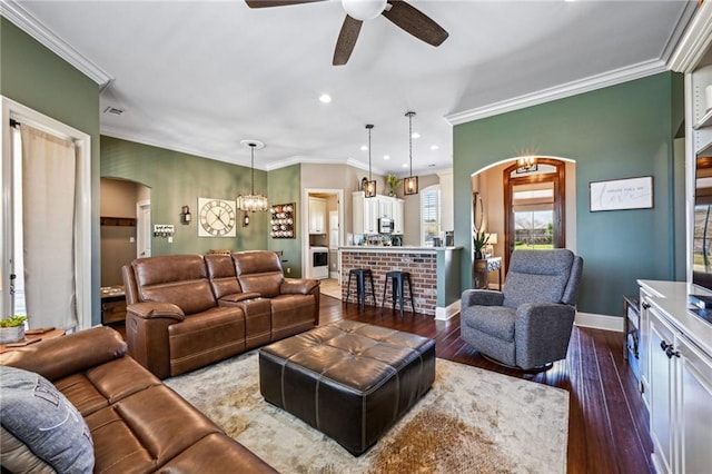 living area with ornamental molding, dark wood finished floors, arched walkways, baseboards, and ceiling fan