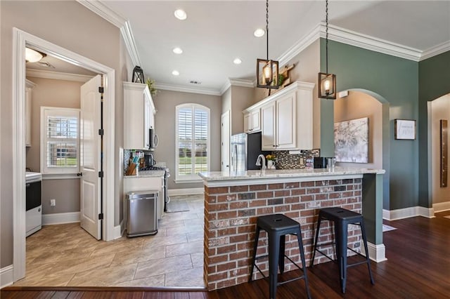 kitchen featuring white cabinetry, freestanding refrigerator, arched walkways, decorative backsplash, and stove