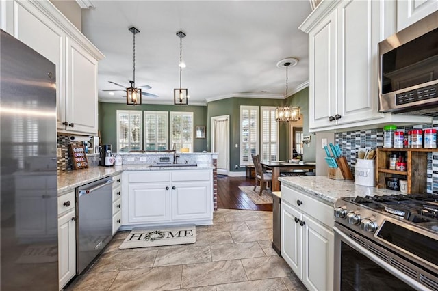 kitchen featuring a sink, stainless steel appliances, white cabinets, ceiling fan with notable chandelier, and backsplash