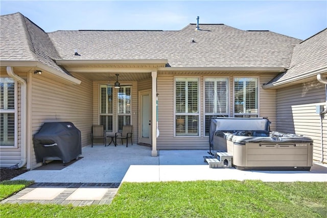 rear view of property featuring a patio area, a shingled roof, and a hot tub