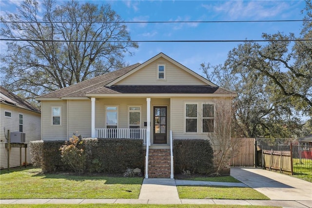 bungalow-style home featuring central air condition unit, a shingled roof, covered porch, fence, and a front lawn