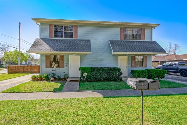 traditional home featuring a shingled roof, fence, and a front lawn