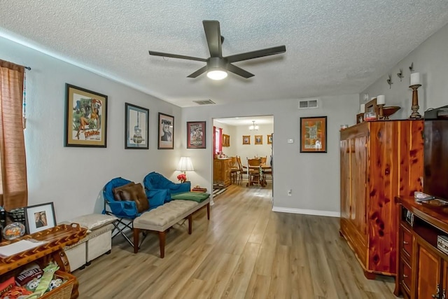 sitting room with a textured ceiling, light wood finished floors, visible vents, and a ceiling fan