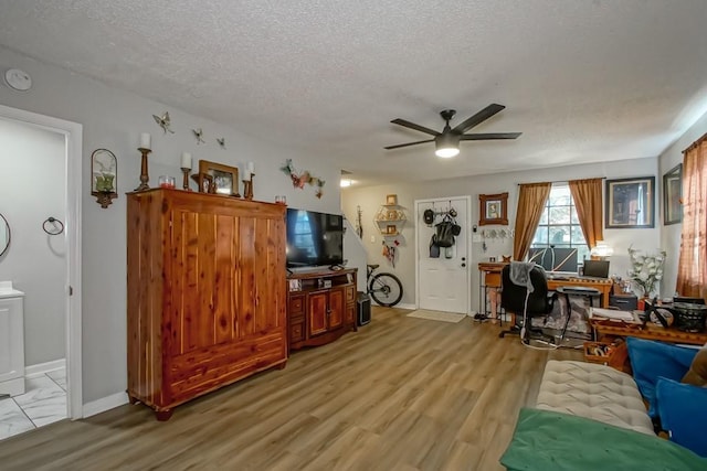 living area featuring light wood-style floors, ceiling fan, a textured ceiling, and baseboards