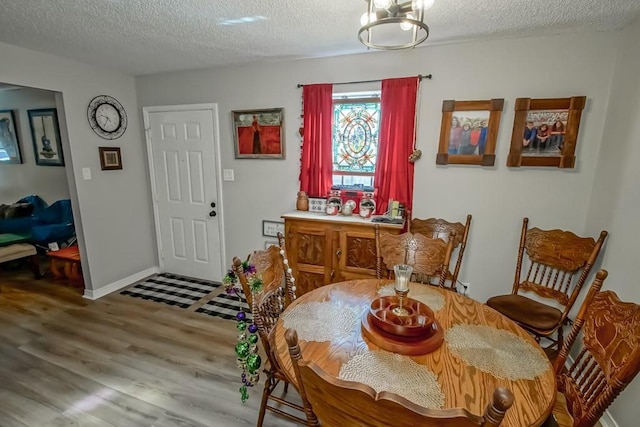 dining area with a textured ceiling, baseboards, and wood finished floors