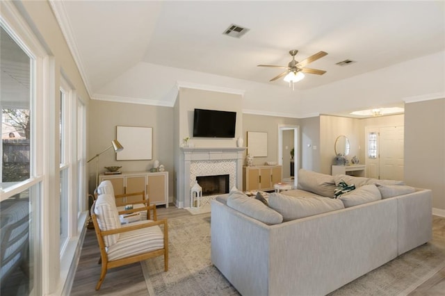 living area featuring light wood-type flooring, a tiled fireplace, visible vents, and crown molding