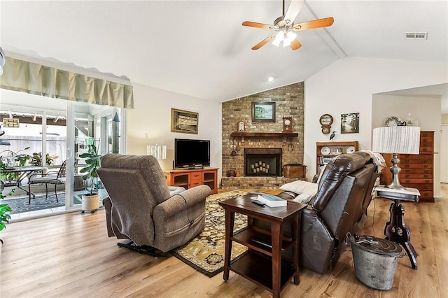 living area featuring vaulted ceiling with beams, a fireplace, visible vents, ceiling fan, and light wood-type flooring