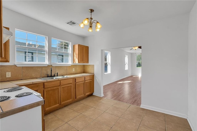 kitchen with light tile patterned floors, tile countertops, a sink, visible vents, and decorative light fixtures