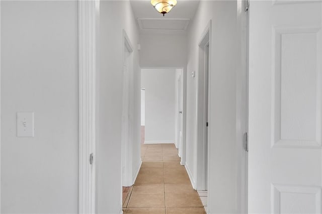 corridor with light tile patterned floors, attic access, and baseboards